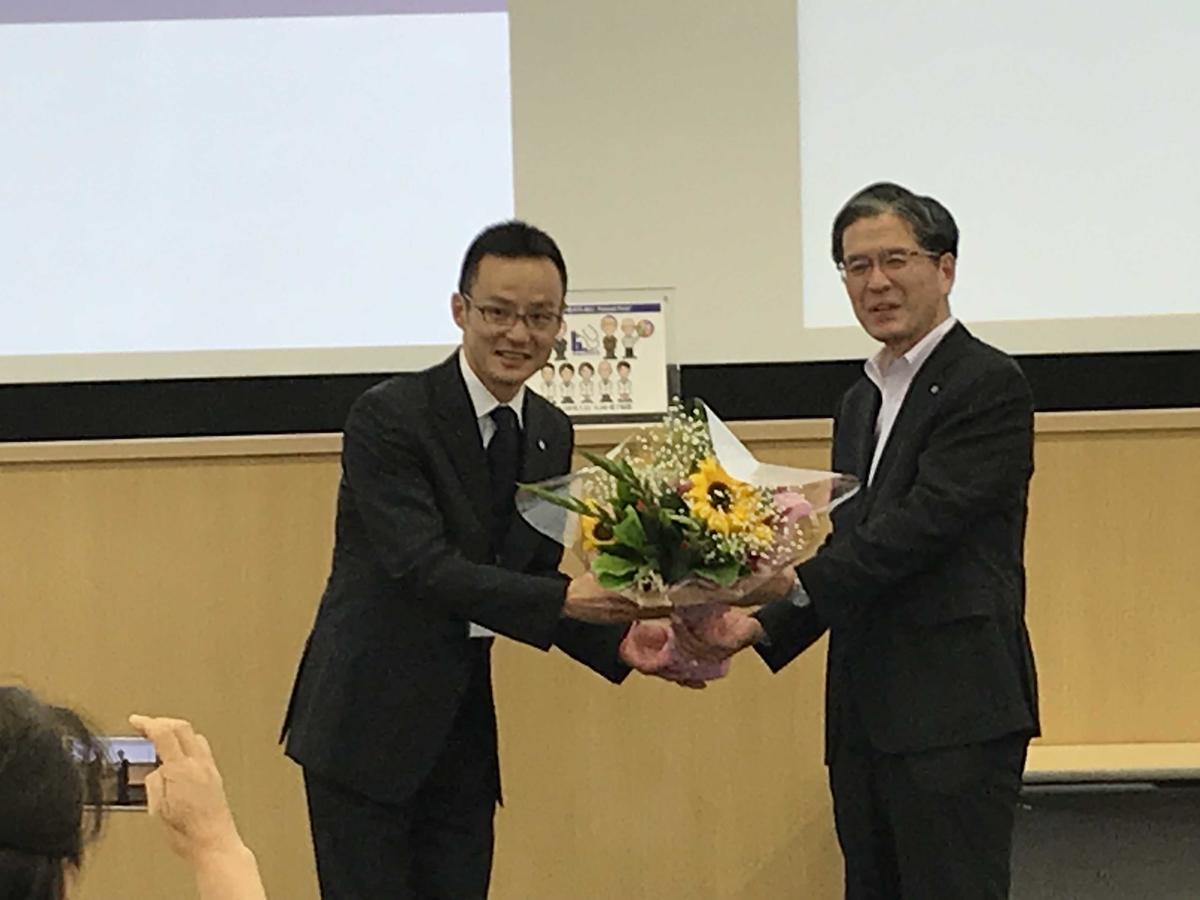 Takeo Furuya (right) receives a bouquet from an ASUISHI graduate at the completion ceremony