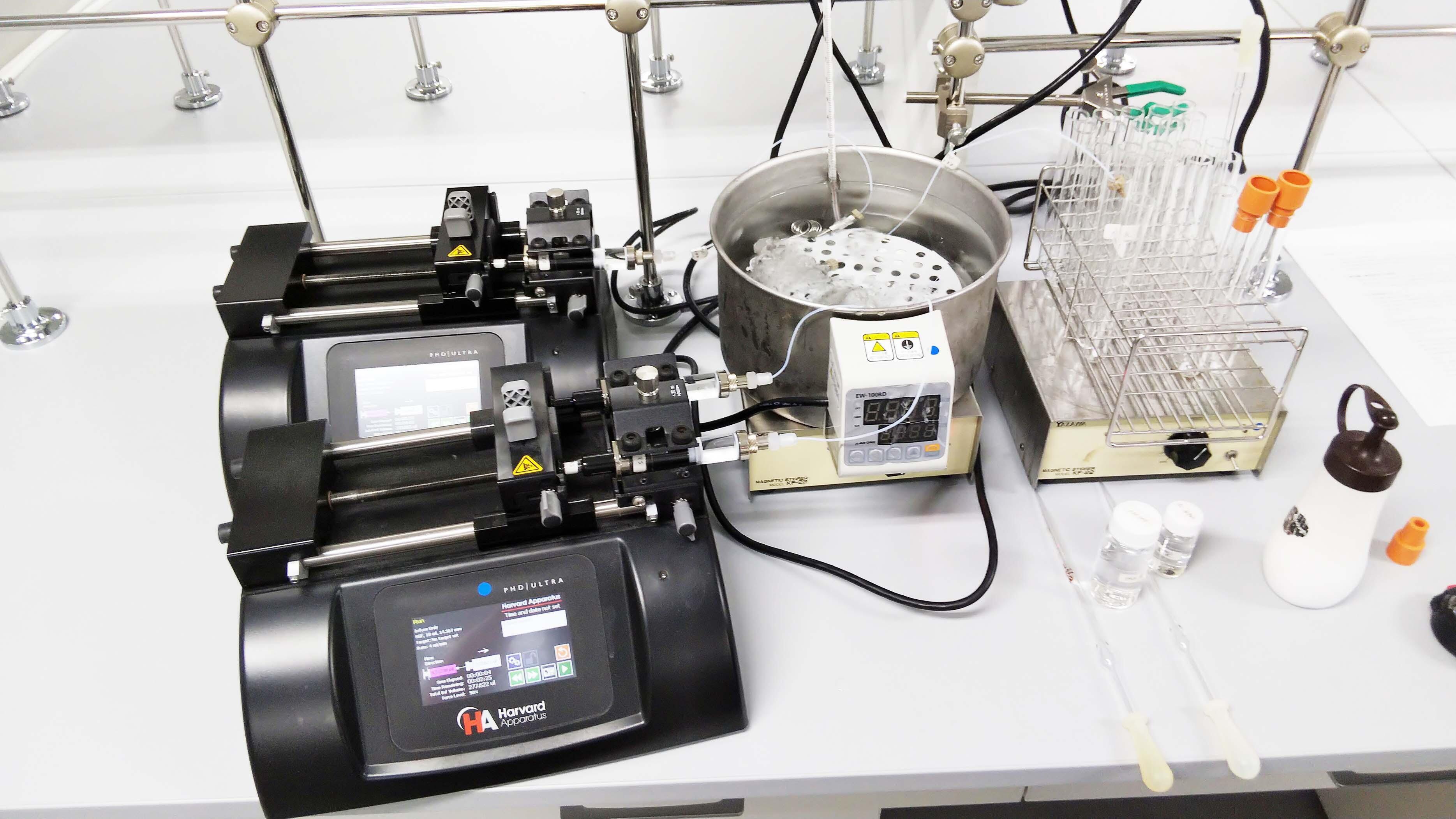 Apparatus for flow reaction experiments. A solution is extruded at a constant rate from the two black devices on the left. The extruded solution is then mixed through tubes in the micromixer.