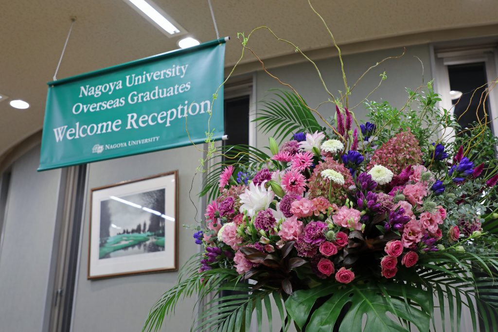 A bouquet of flowers celebrating the occasion stands next to a green banner reading "Nagoya University Overseas Graduates Welcome Reception"