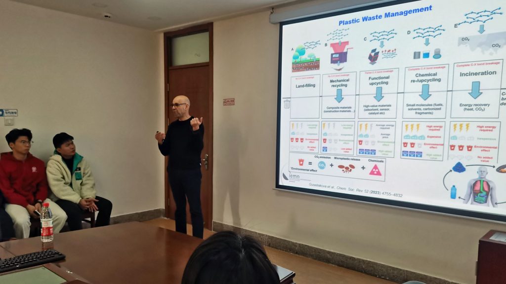 A professor stands at the front of a room explaining a diagram projected on a screen.