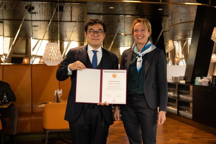 Nagoya University Professor Hiroshi Nishikori, holding a certificate honoring his selection as a KIPRIME Fellow, stands next to another person.