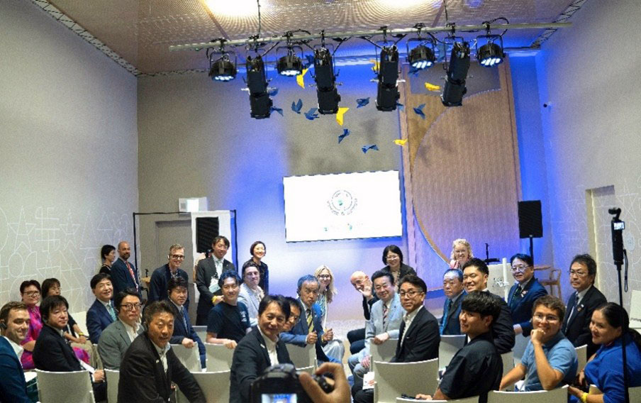 Participants at the badge ceremony turn around in their seats for a group photograph shot from the back of the room.