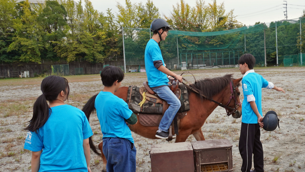 One student rides a Kiso horse while three other students stand nearby