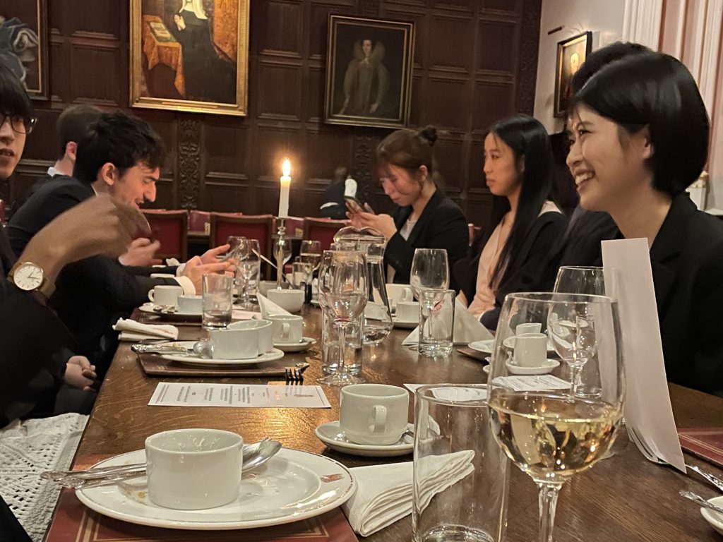 Students sit on either side of a long, dark wood table during the formal dinner.