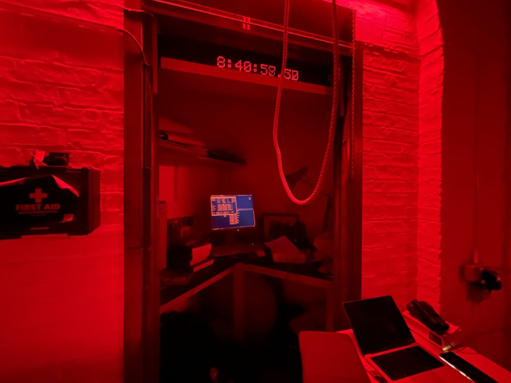 A computer sits in the middle of an angled desk in the control center for the telescope; the whole room is bathed in a red light.