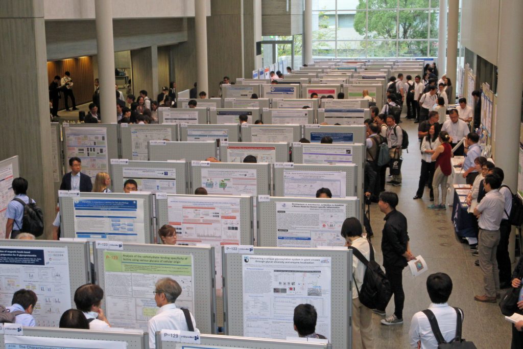 Participants walk around the lobby of Toyoda Auditorium, which has been filled with poster displays.