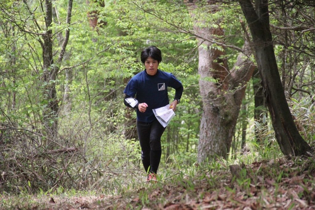 A student runs through the forest holding a map, looking for the next control.