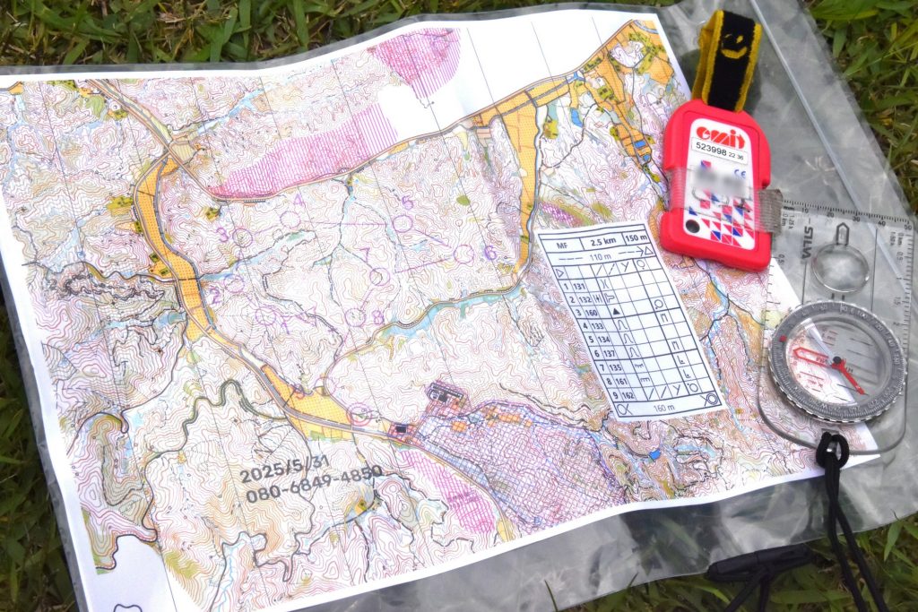 A photograph of an open orienteering map with a compass and one of the cards that students use to log their times.