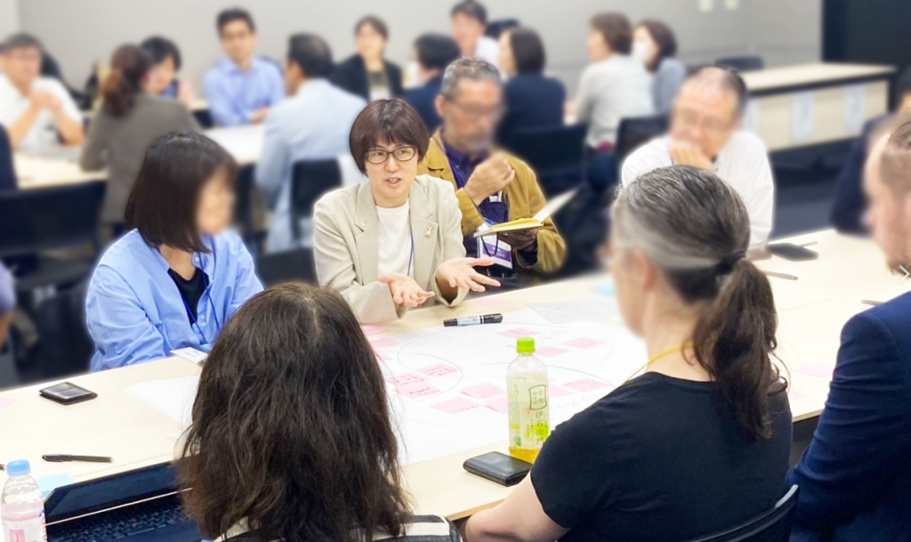 A photo from the 11th Annual RA Conference; participants sit on both sides of a long rectangular tables brainstorming a topic.