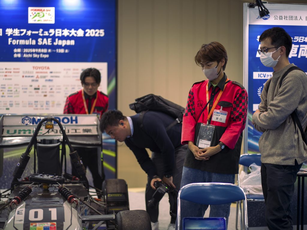 Nagoya University students and attendees stand around the formula car.