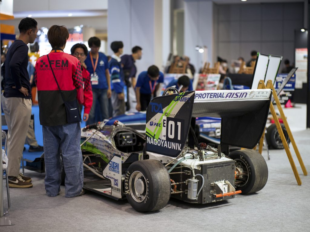 A Nagoya University student and attendees stand around the formula car.