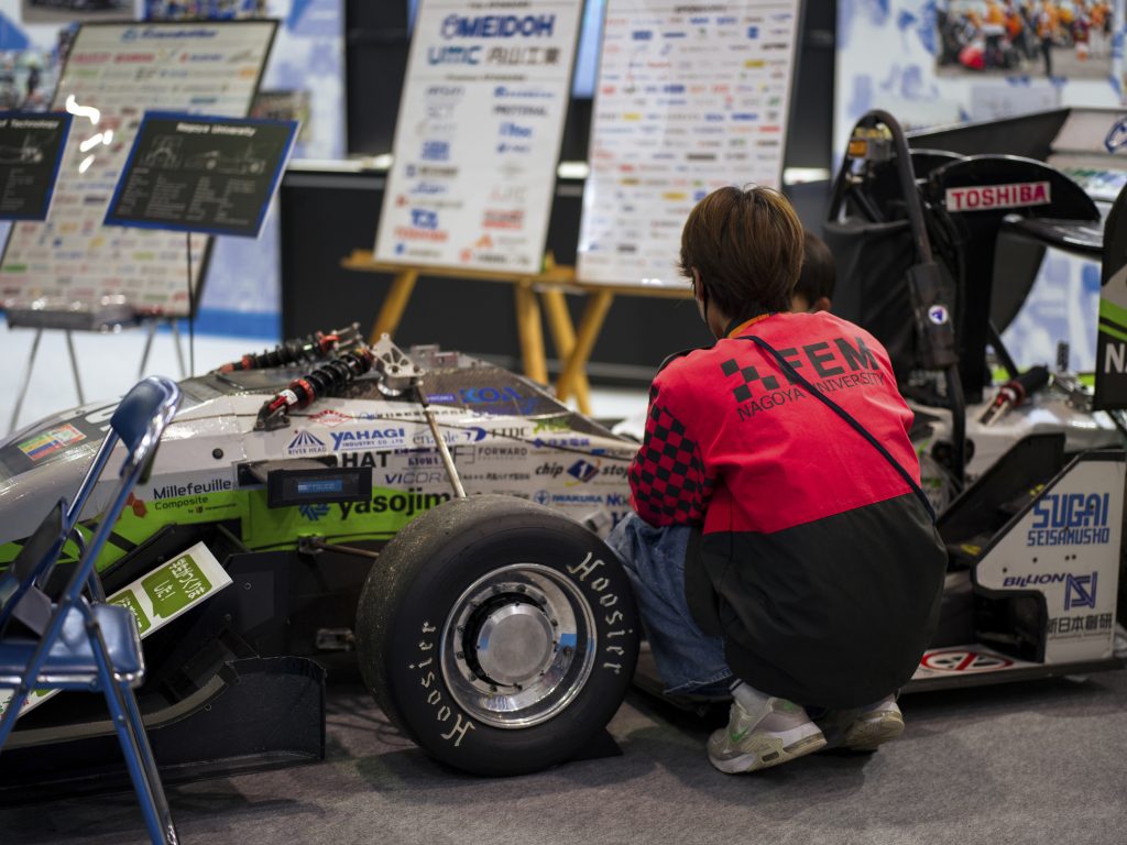 A Nagoya University student crouches next to the formula car.