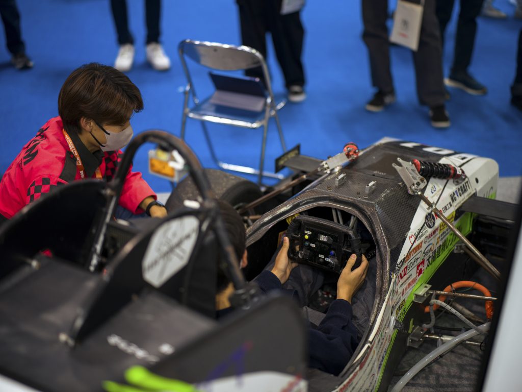 A Nagoya University student helps an attendee sit in the formula car.