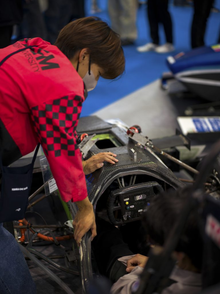 A Nagoya University student helps an attendee sit in the formula car.