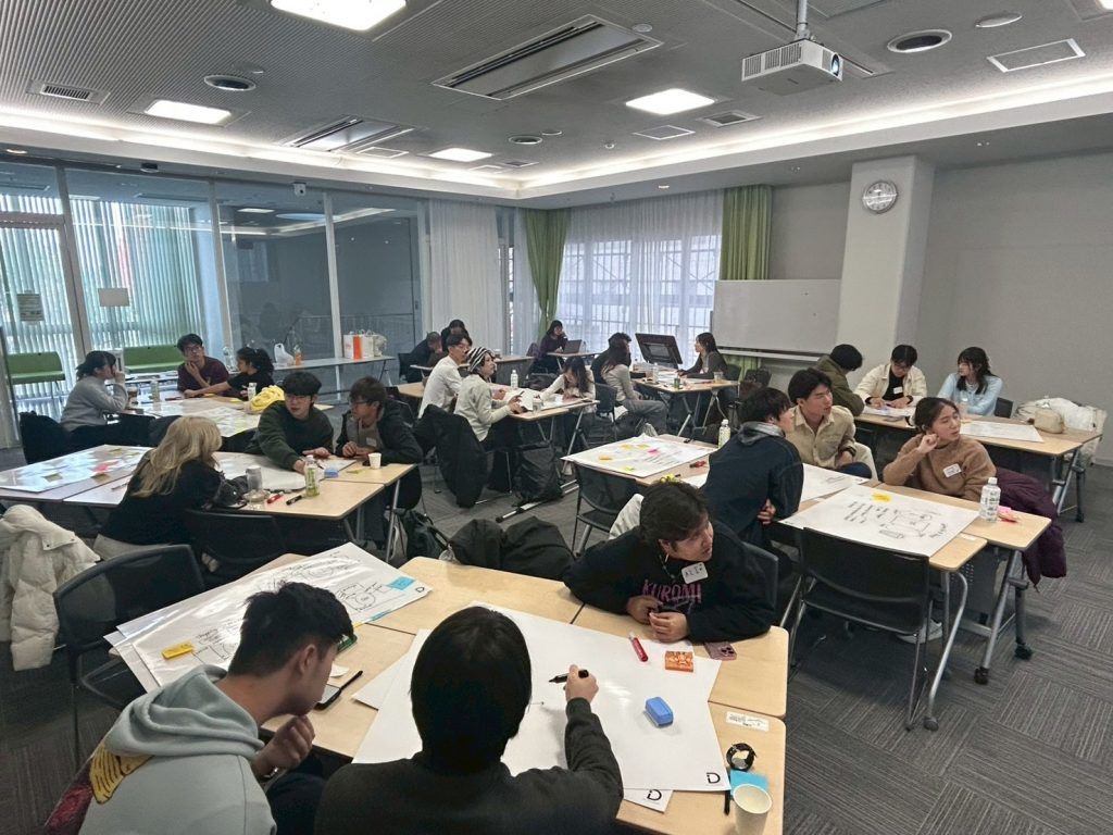 Students sit in groups at tables working on creating a poster during the workshop.
