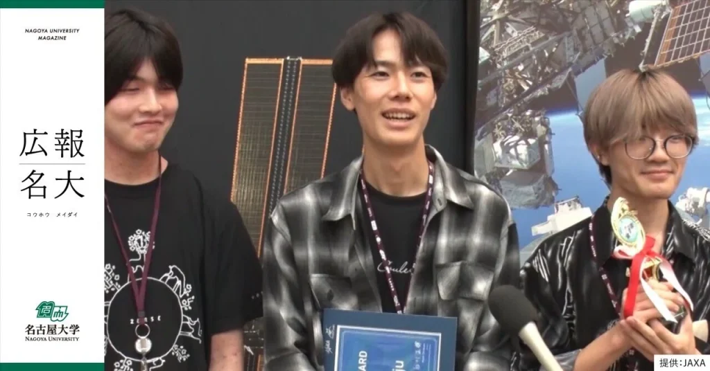 Ishiwatari, a student in his early 20s, stands between his team members. He is holding an award.