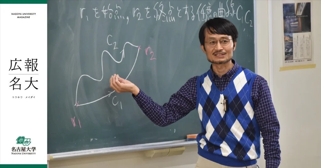 Professor Tanimura points to a diagram on a chalkboard. He wears glasses and a sweater vest with a blue and white diamond pattern.