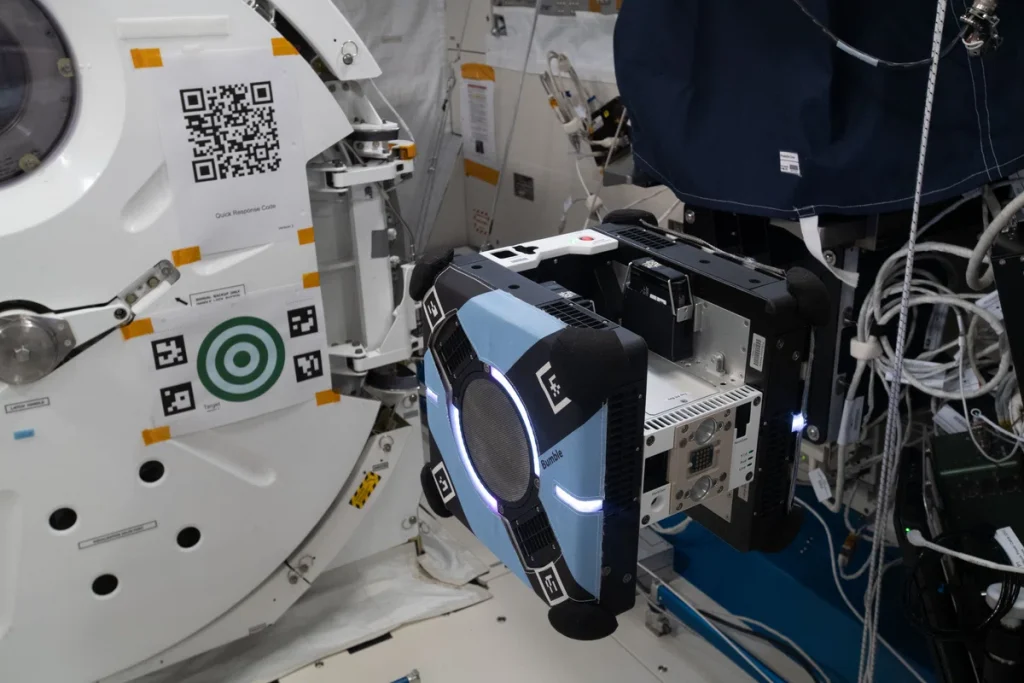 A photograph of a blue cube-shaped drone in flight.