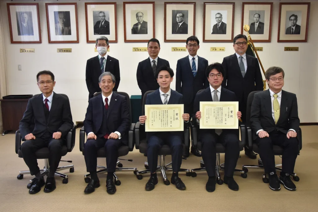 A group photo with prize committee members etc. President Sugiyama and awardees Tanaka and Yamamoto sit side-by-side in the front row.