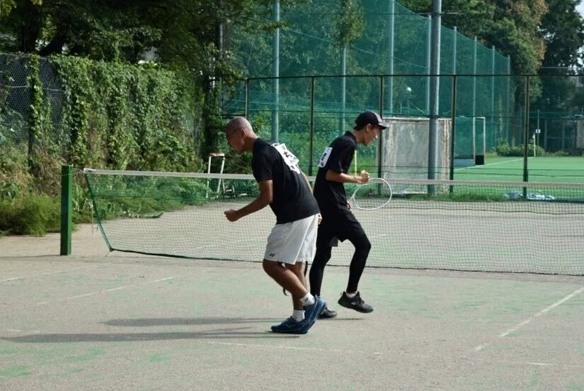 Ishiwatari and a team member make a celebratory pose on a tennis court.