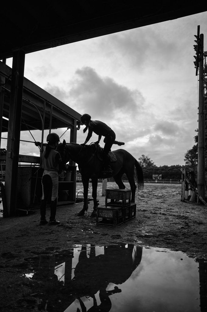 Monochrome picture of a student climbing upon a horse during preparation phase