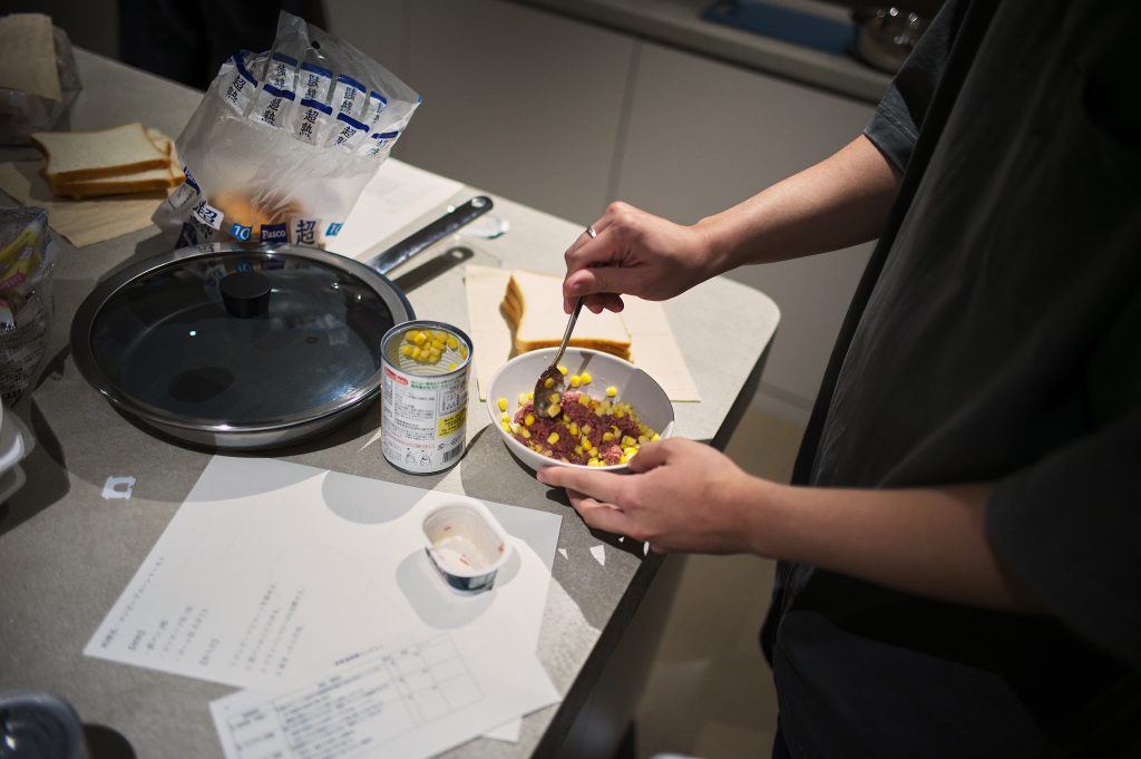 Student prepares corn beef and canned corn mixture in a bowl for sandwich making